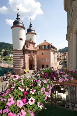 Two historic towers with weather vanes stand proudly atop this charming building, featuring a grand archway entrance and a beautifully adorned balcony.