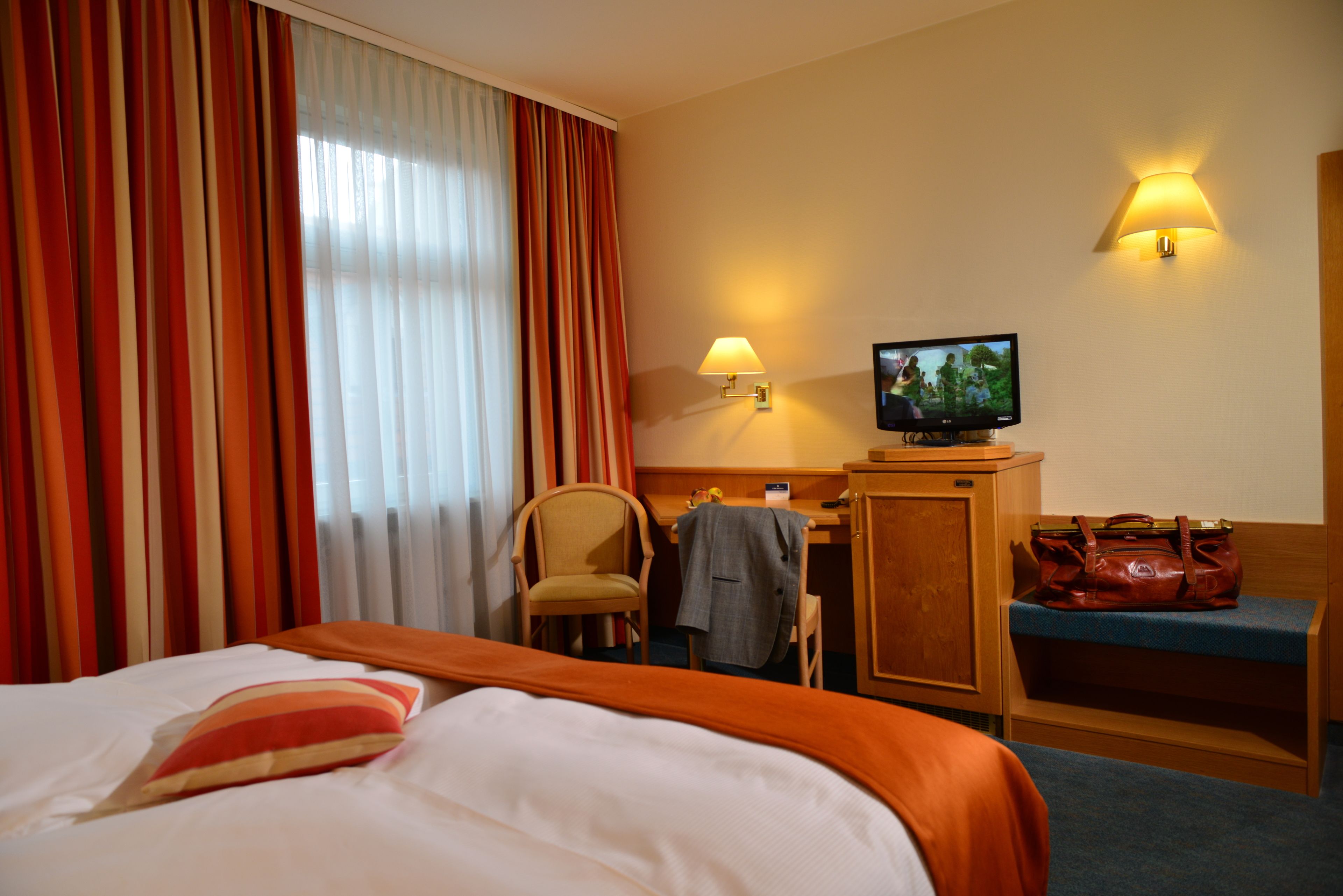 A hotel room with a bed, a desk, a television, a chair, and a bench.