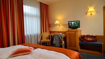 A hotel room with a bed, a desk, a television, a chair, and a bench.
