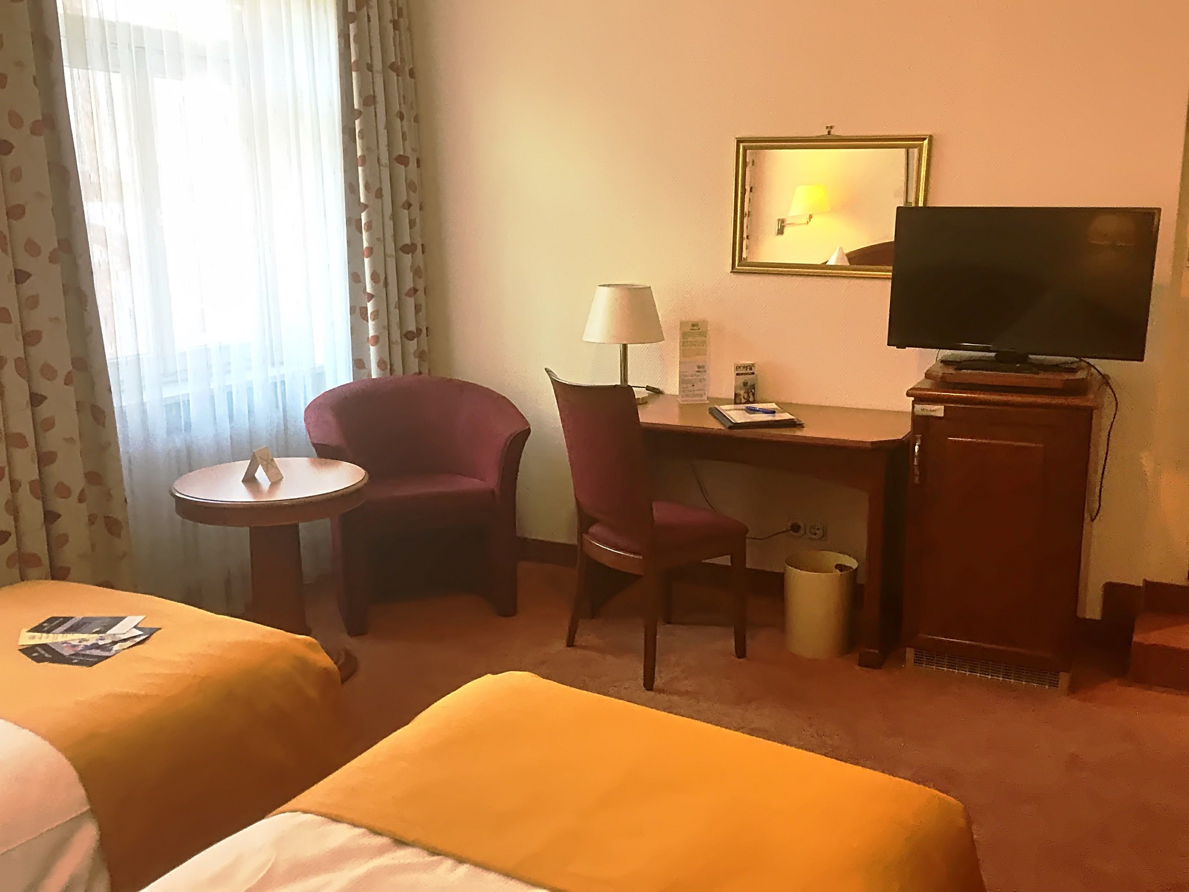 Habitación de hotel con dos camas, un escritorio con silla, un televisor y una mesita.