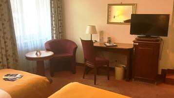 A hotel room with two beds, a desk with a chair, a television, and a small table.