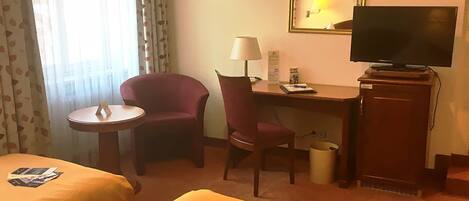Habitación de hotel con dos camas, un escritorio con silla, un televisor y una mesita.