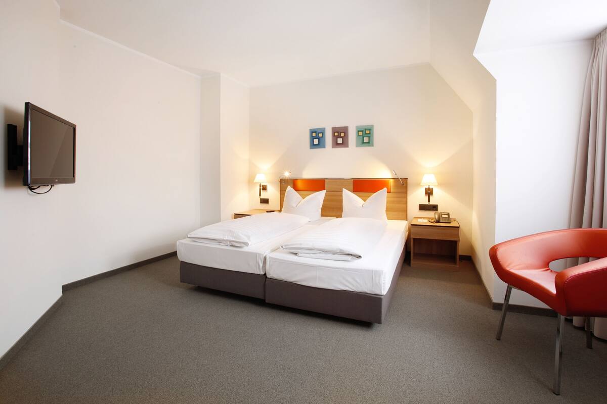 A hotel room with a bed, two bedside tables, a TV, and a red chair.