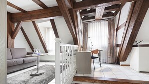 A loft-style room with exposed wooden beams, a white railing, a sofa, a small table, and a red rug. - Hotel am Jakobsmarkt (Nuremberg)