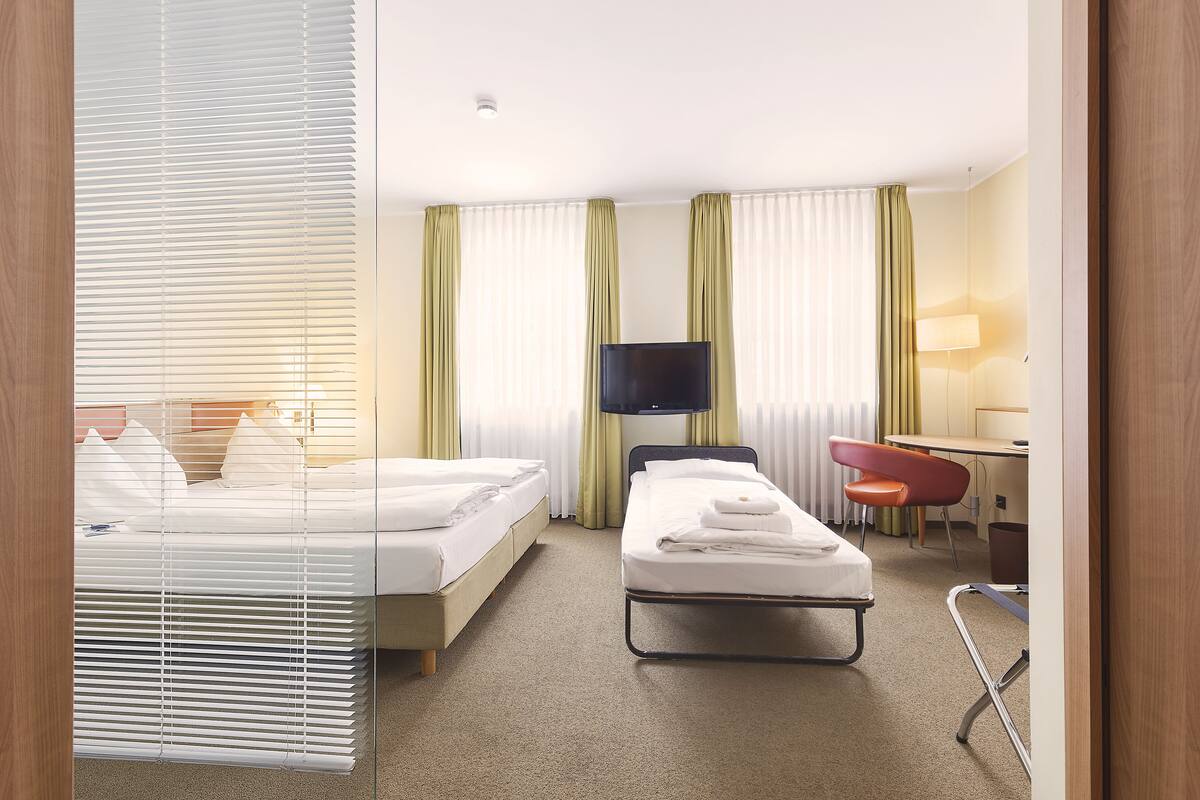 A hotel room with two beds, a desk, a chair, and a TV.