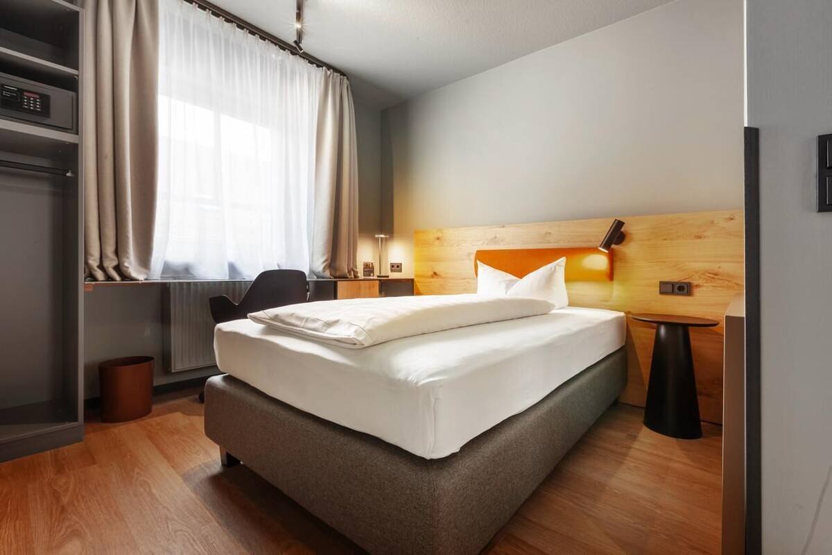 A modern hotel room with a large bed, a desk, a chair, and a small table.