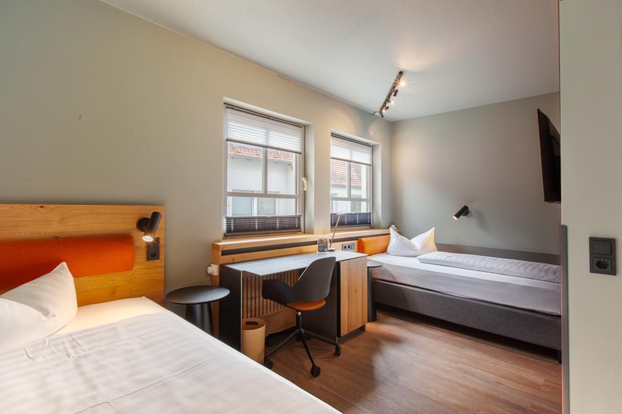 Une chambre d’hôtel de taille réduite, comprenant un lit, un bureau et un petit coin salon.