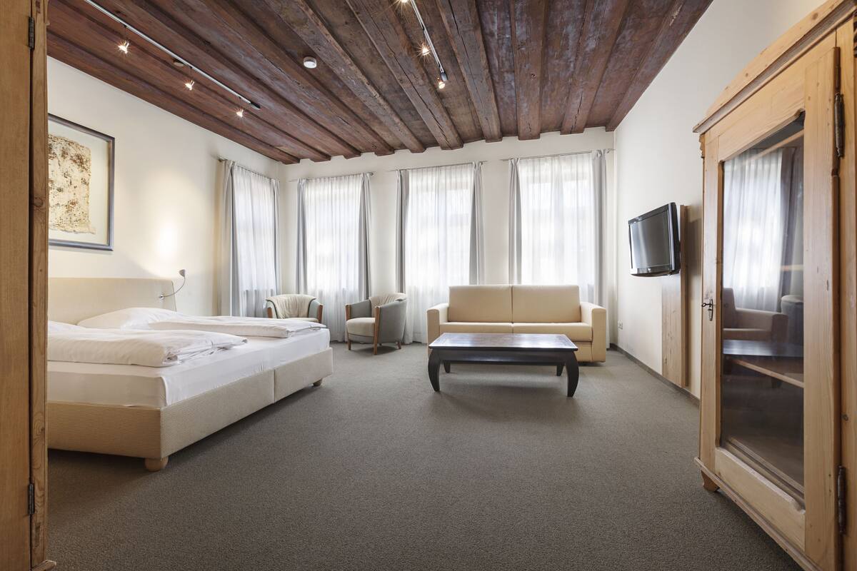 A modern room with a wooden ceiling, a sofa, a bed, a TV, and a cabinet.