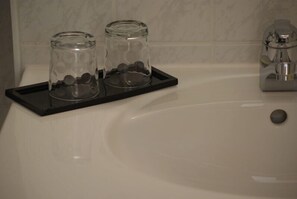 Casa de banho com um tabuleiro preto que contém dois frascos de vidro cheios de objetos redondos, uma banheira branca e uma torneira prateada.