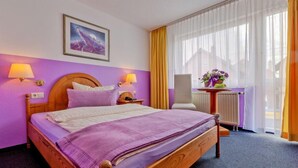 A hotel room with a large bed, two bedside lamps, a painting on the wall, a window with curtains, and a small table with a vase of flowers. - Hotel Freihof (Stuttgart)