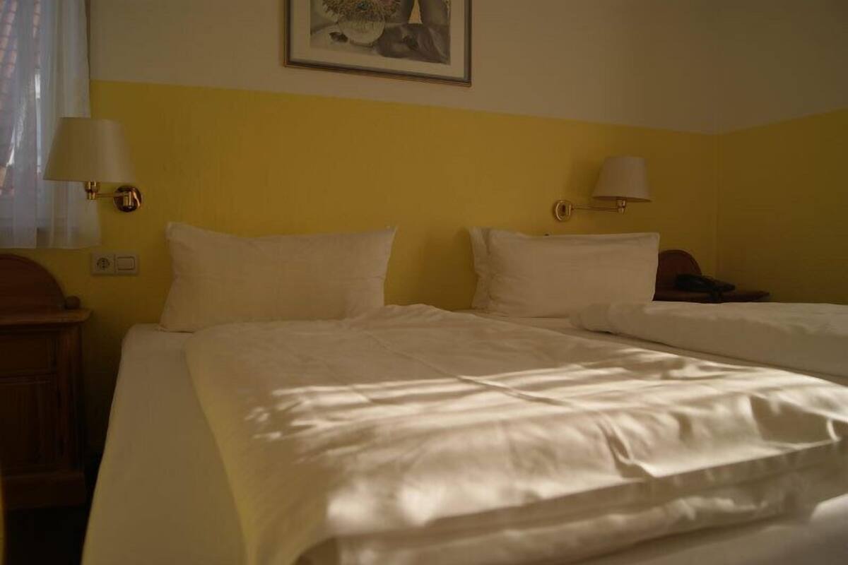 A hotel room with two beds, each with white bedding and lamps on either side.