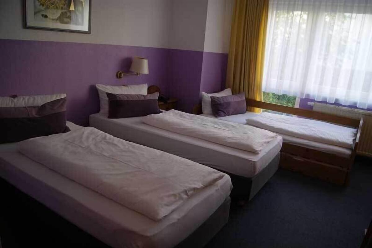 A hotel room with two single beds, a small table, a lamp, and a window with curtains.