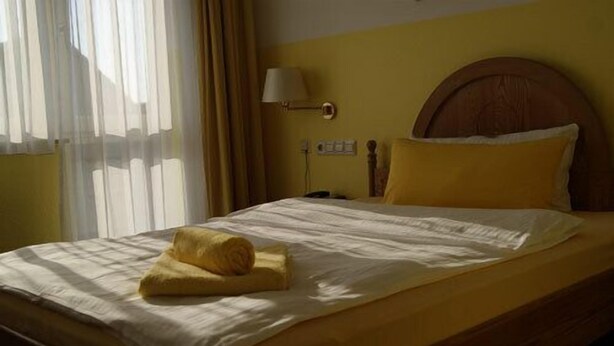 A bed with a wooden headboard, a yellow pillow, and a rolled towel on the bed. - Hotel Freihof (Stuttgart)