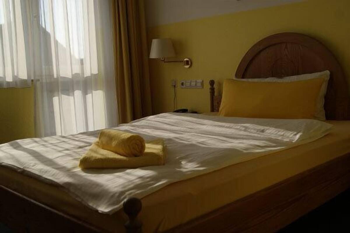 A bed with a wooden headboard, a yellow pillow, and a rolled towel on the bed.