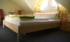 A single bed in a room with a sloped ceiling, a small bedside table, a lamp, and a window with curtains. - Hotel Freihof (Stuttgart)