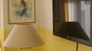 A room with a TV mounted on the wall, a framed painting above it, and a lamp with a beige shade. - Hotel Freihof (Stuttgart)