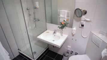 Un baño moderno con ducha envuelta en vidrio, un lavabo blanco con espejo arriba y un inodoro.