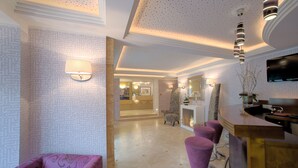 Un vestíbulo moderno de hotel con papel tapiz estampado, una zona de bar con taburetes morados y un mostrador de recepción.