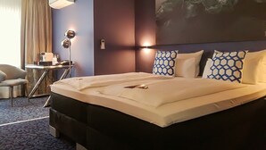 Una habitación de hotel con una cama grande, un escritorio con lámpara y un cuadro en la pared.