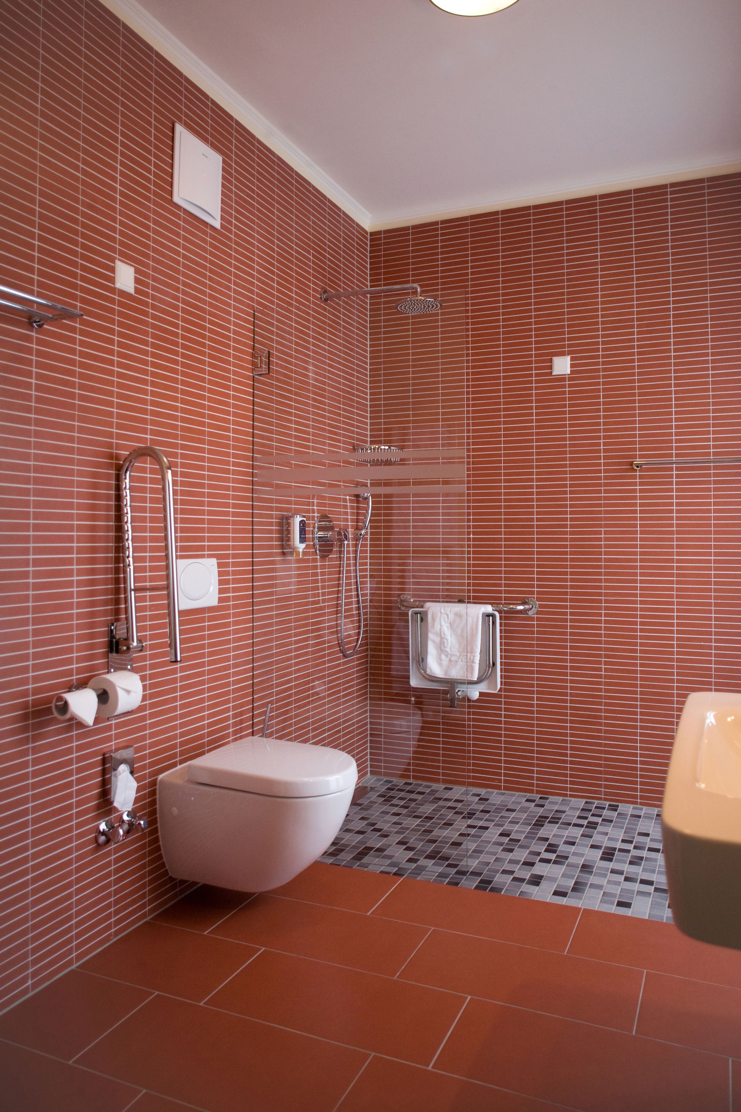Uma casa de banho com parede revestida a azulejos vermelhos, sanita branca, área de duche e secador de mãos.