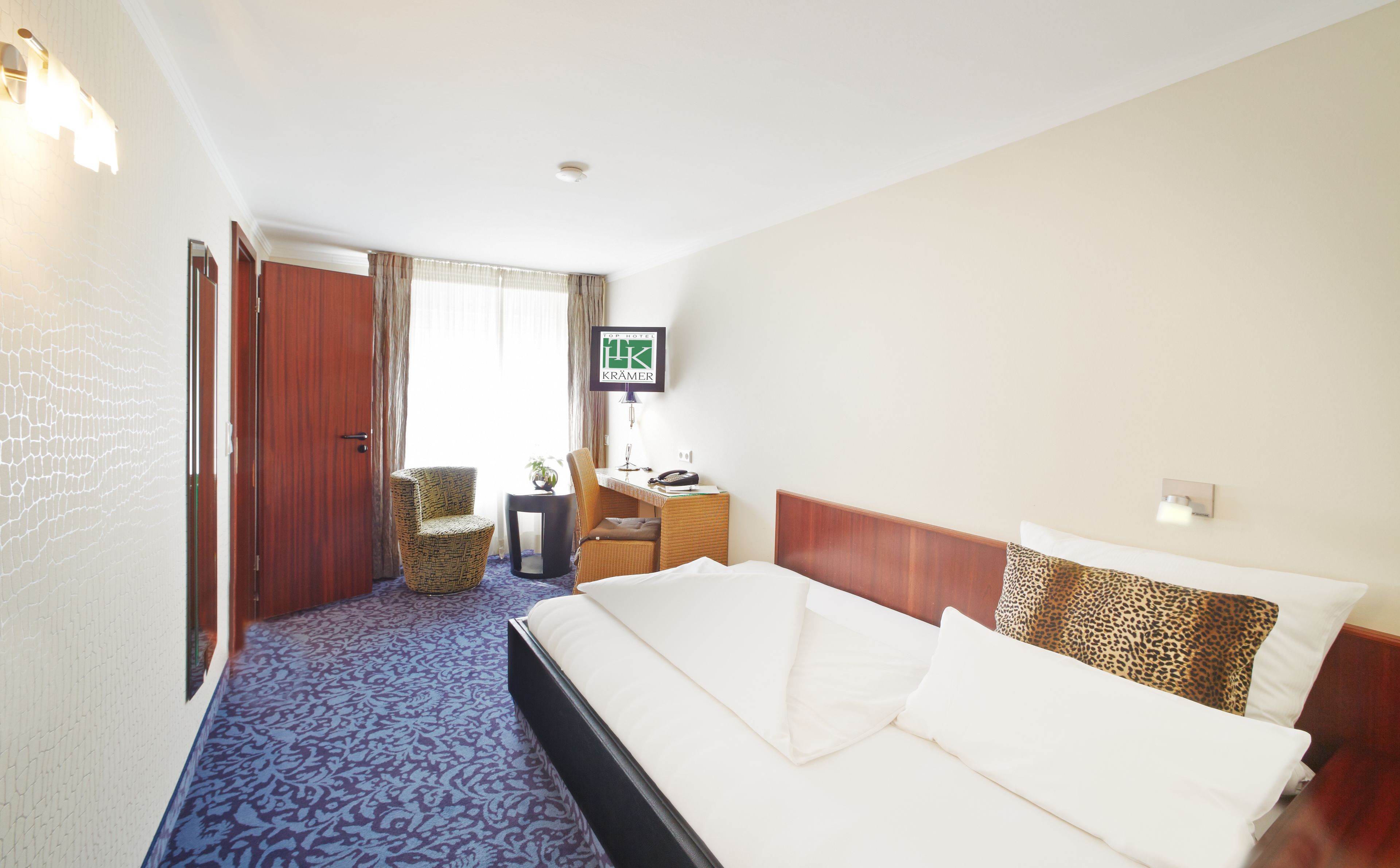 Ett hotellrum med en stor säng, ett skrivbord med en telefon, en stol och en tv på väggen.