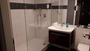 A modern bathroom with a glass shower enclosure, a white sink with a dark cabinet, and a toilet.