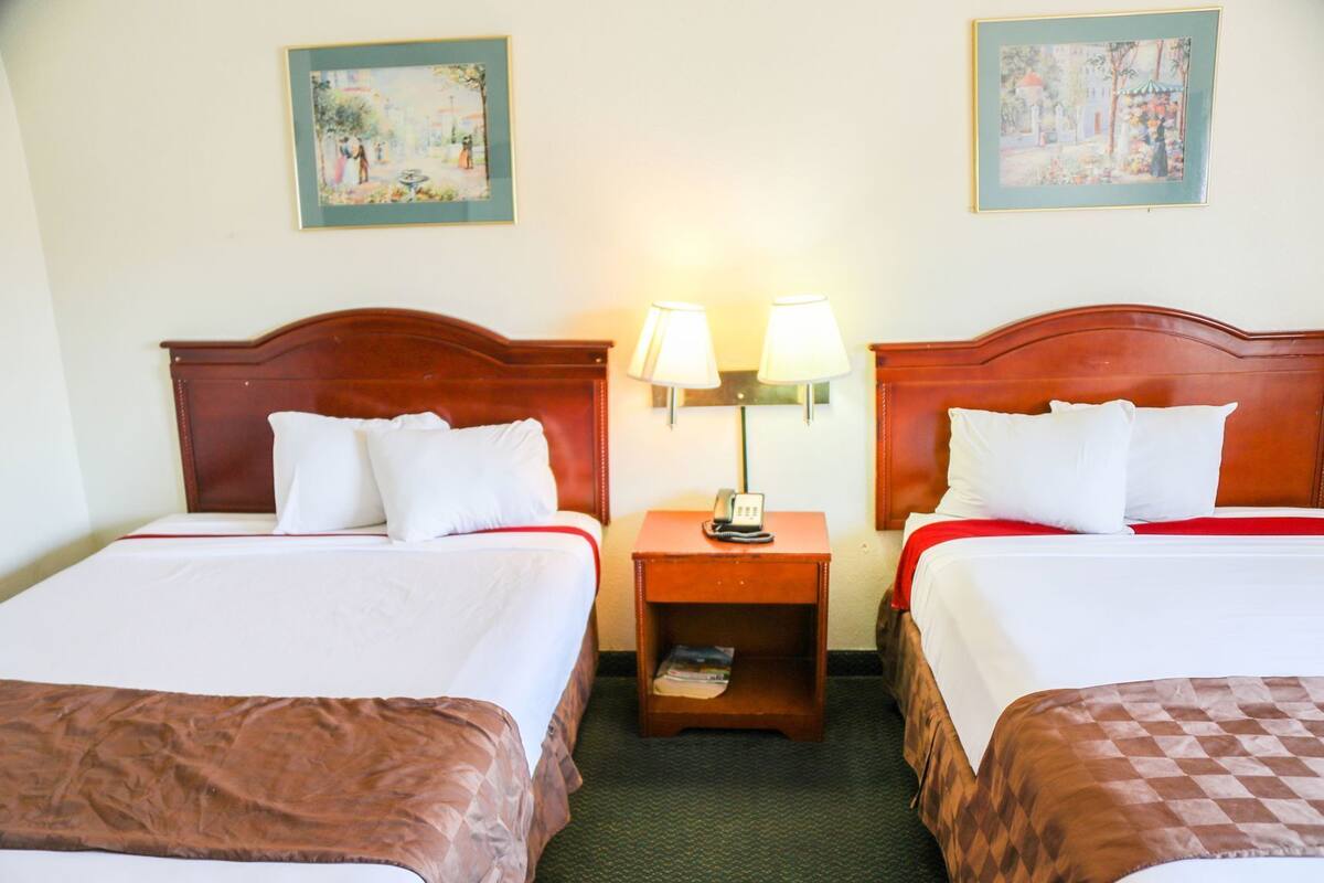 A hotel room with two beds, a nightstand with a lamp, and two framed pictures on the wall.