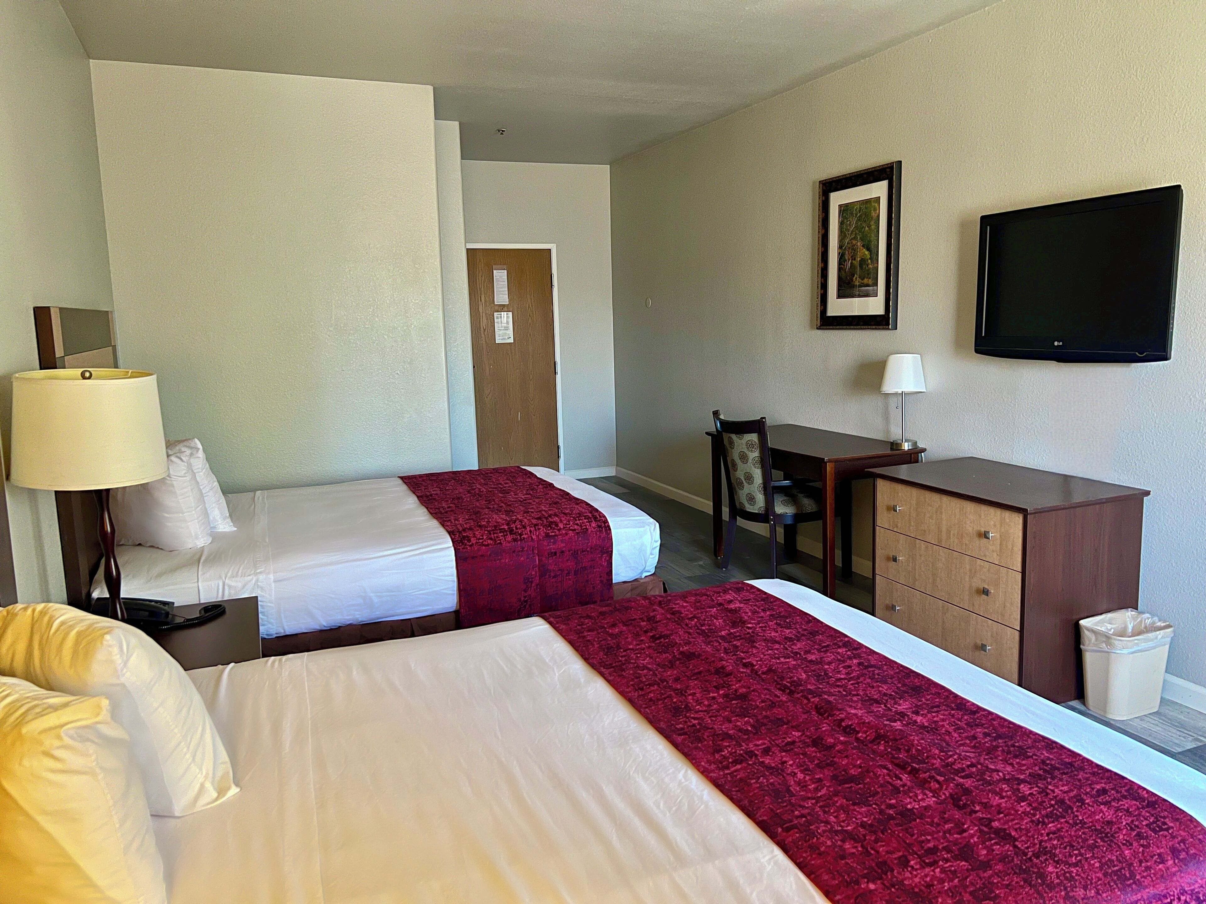 Une chambre d’hôtel avec deux lits, un bureau, une chaise, une télévision et une poubelle.