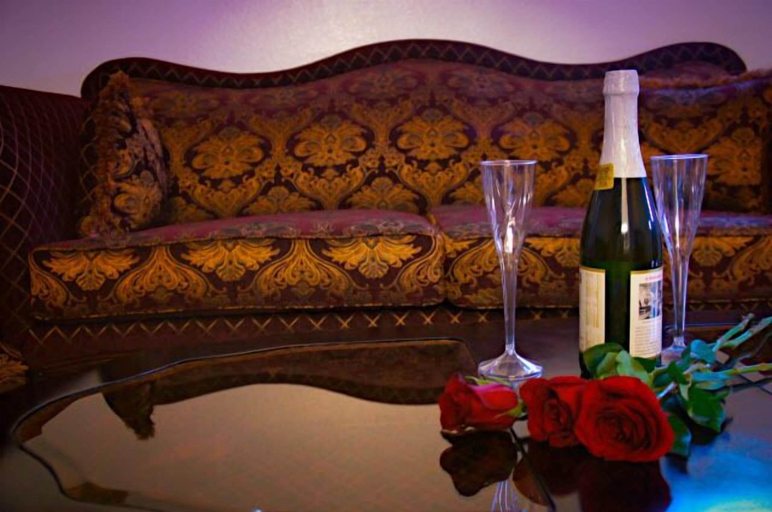 Une pièce avec un canapé à motifs, une table sur laquelle se trouve une bouteille de vin, deux verres et un bouquet de roses.