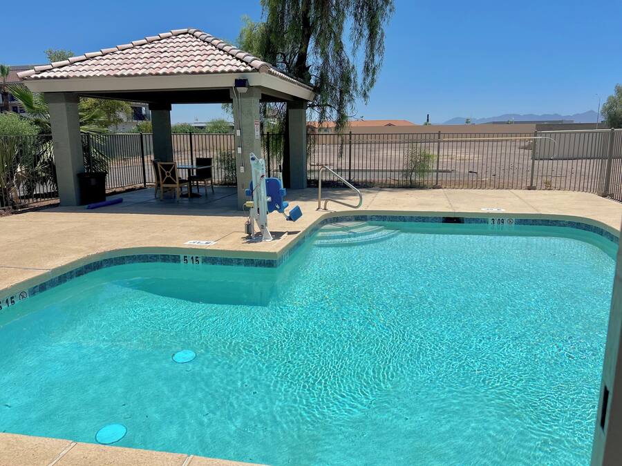 A clear swimming pool with a tiled deck area, a gazebo, and a fenced yard.