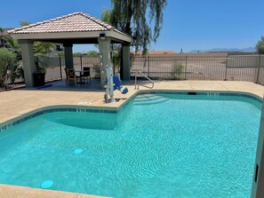 A clear swimming pool with a tiled deck area, a gazebo, and a fenced yard.
