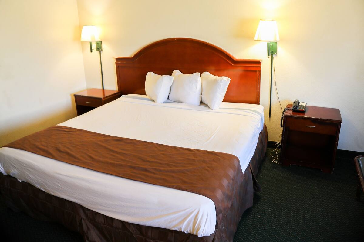A hotel room with a large bed, two bedside tables, a nightstand with a telephone, and two wall-mounted lamps.