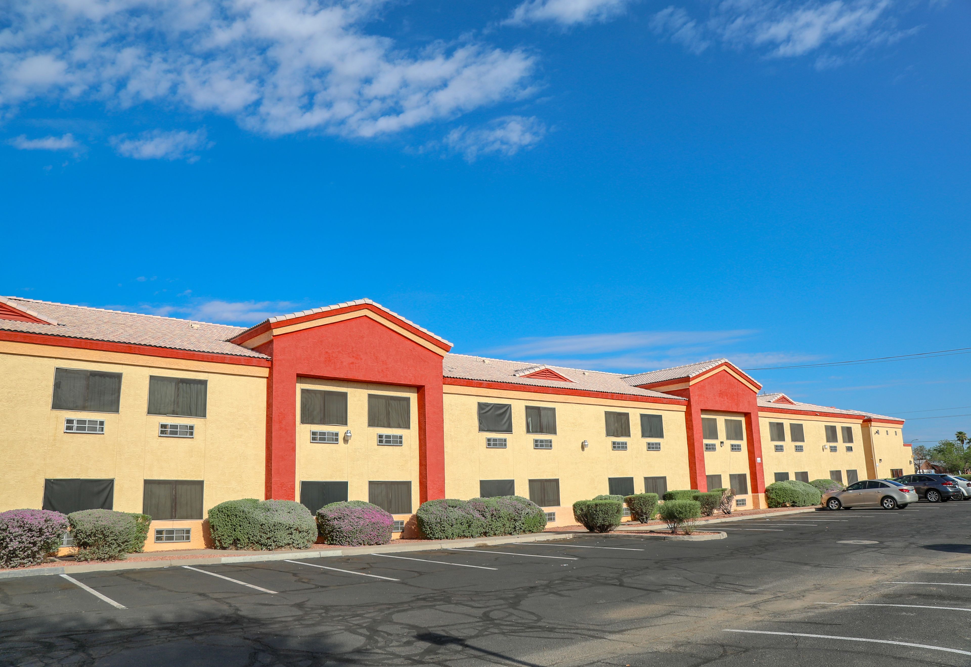 A hotel with a row of rooms, a parking lot, and a clear blue sky.
