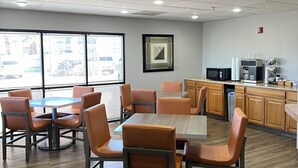 A conference room with a large table and chairs, a kitchenette, and a window with blinds.