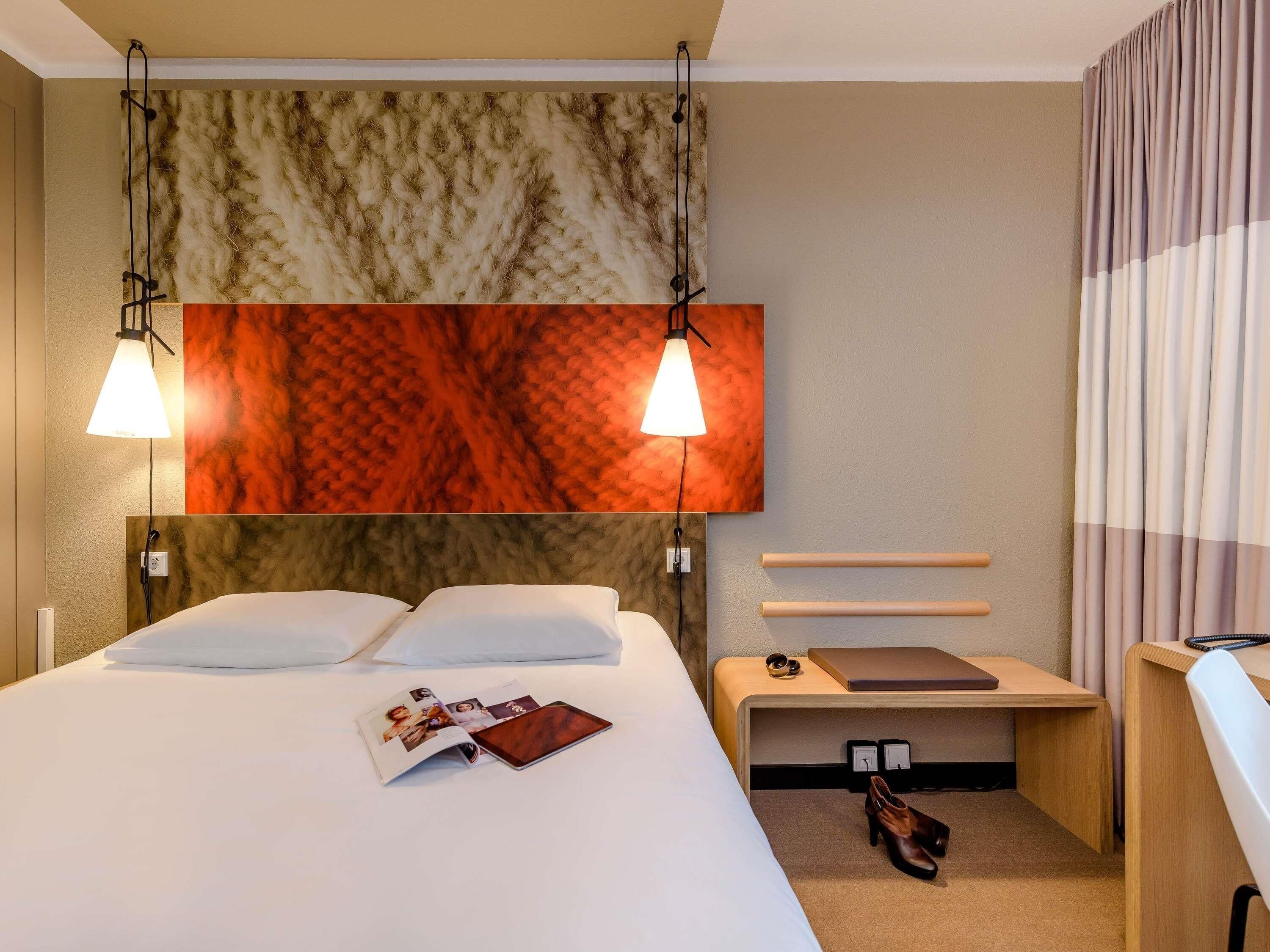Ein Hotelzimmer mit Bett, Nachttischen, einem Schreibtisch und einer Wandlampe.