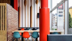 A modern dining area with a wooden partition, colorful chairs, and a large red pillar. - ibis Muenster City (Münster)