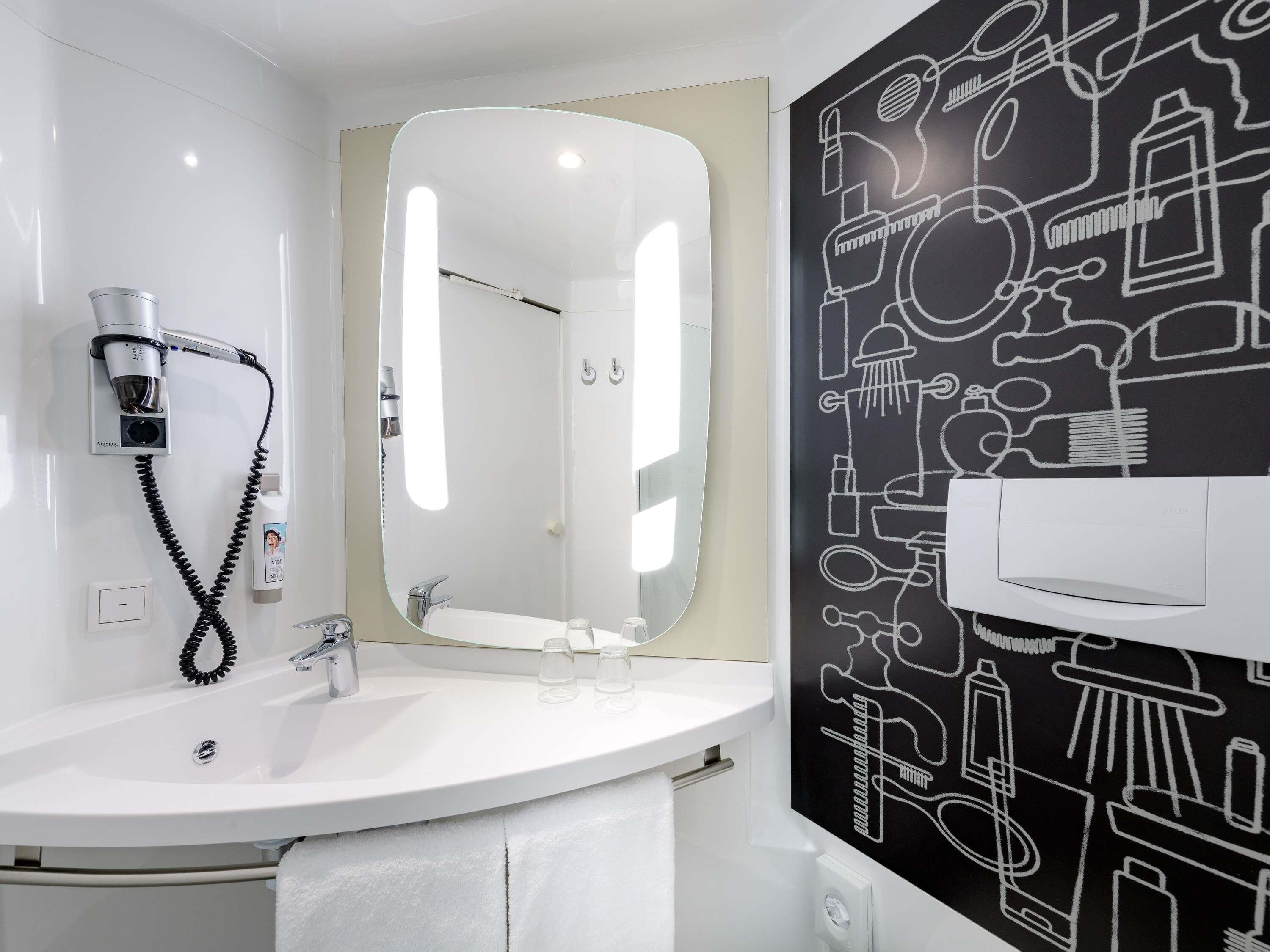 A modern bathroom with a white sink, a hairdryer, a mirror, and a wall with black and white bathroom-related illustrations.