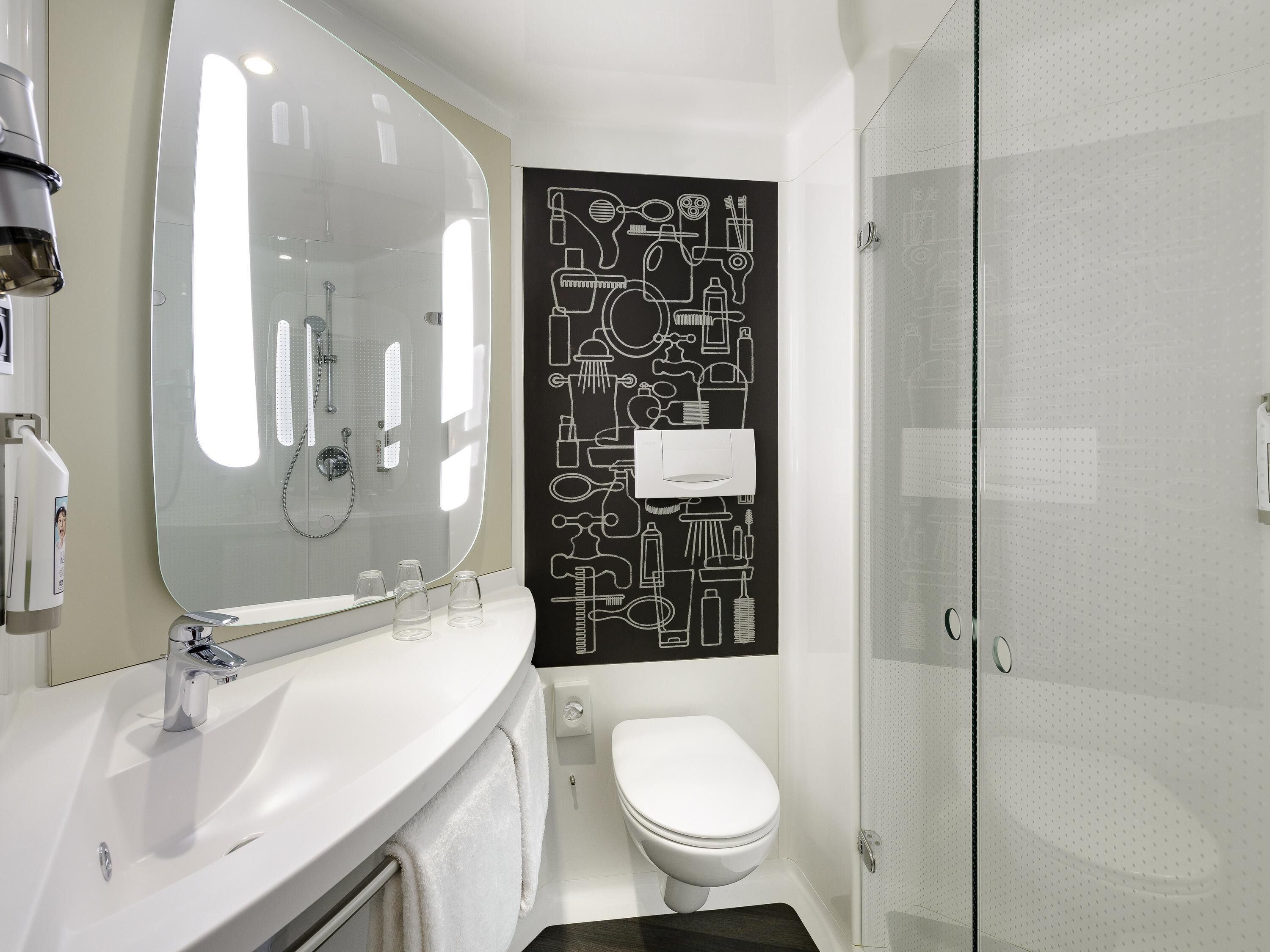 A modern bathroom with a large mirror, a white sink, a toilet, and a shower enclosure.