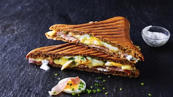 A sandwich cut in half with visible fillings and a small bowl of sauce.