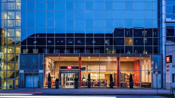 A modern hotel with a glass facade, a visible entrance, and outdoor seating area. - ibis Muenster City (Münster)