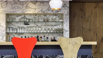 Un coin bar avec un mur décoré de motifs, des étagères remplies de verres et deux chaises.