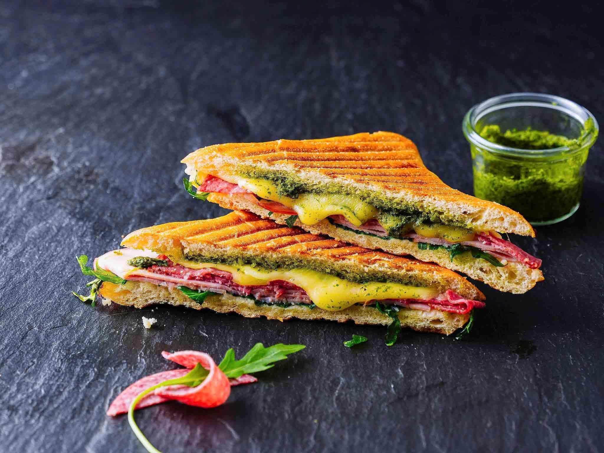 A sandwich with multiple layers, a glass of green sauce, and a sprig of parsley on a dark surface.