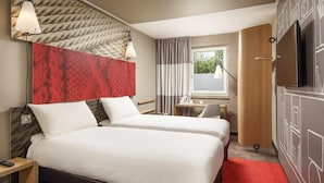 A hotel room with a bed, bedside tables, a desk, a chair, a TV, and a window. - ibis London Stratford (London)