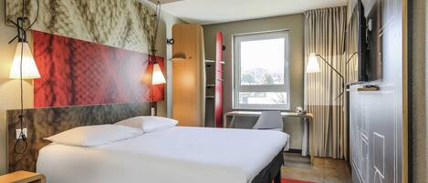 A hotel room with a bed, bedside lamps, a TV, a window, and a red carpet.