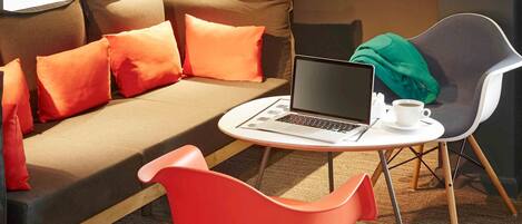 Une chambre d’hôtel moderne avec un canapé, un fauteuil rouge, un ordinateur portable et une tasse de café sur une petite table.