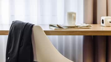 Una silla moderna con una chaqueta negra apoyada, una taza blanca y un dispositivo blanco sobre una mesa de madera.