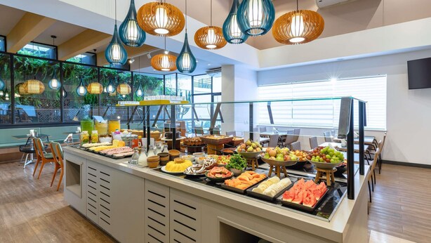 A buffet with a variety of food items, a glass partition, and hanging pendant lights.