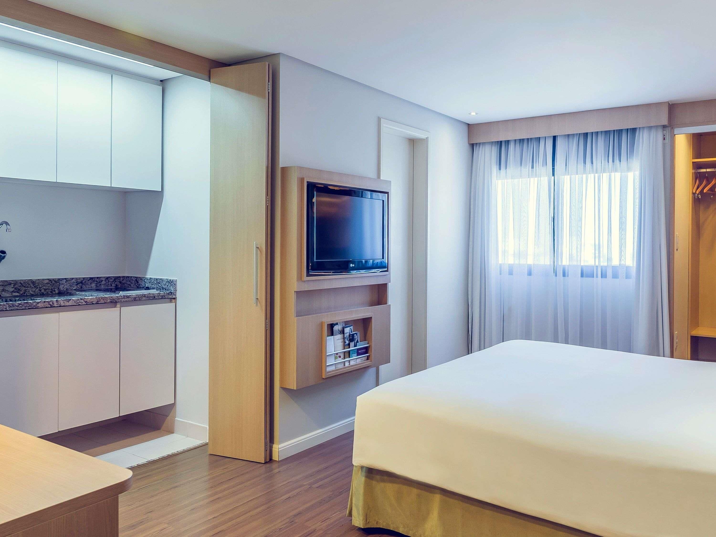 Une chambre d’hôtel équipée d’un lit, d’une télévision, d’un minibar, d’une salle de bain et d’une fenêtre avec des rideaux.