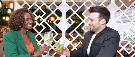 Two people seated at a table with drinks, in front of a white decorative partition.