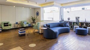 A modern lounge area with a curved blue sofa, green armchairs, a small table, and a potted plant.